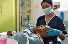 a woman wearing a mask and gloves is working on a man 's teeth