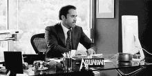 a man in a suit and tie is sitting at a desk with a sign that says aquafina .