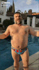 a shirtless man in swim trunks is standing next to a swimming pool