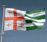 a green white and orange flag with a cross on it is flying in the wind