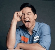 a man in a blue shirt is sticking his tongue out while making a funny face .
