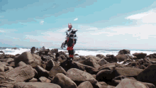 a man in a superhero costume stands on a rocky beach