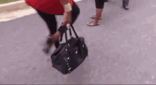 a woman is carrying a black purse while walking down a street