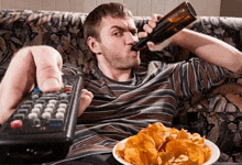 a man sits on a couch holding a remote control and a bottle of beer