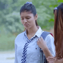 a girl wearing a tie and a white shirt is standing next to another girl with a backpack .