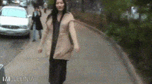 a woman is walking down a sidewalk with a car in the background and the words imodelina on the bottom right