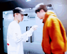 a man wearing an orange hoodie talks to another man in a baseball cap