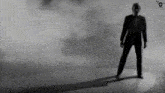 a black and white photo of a man in a suit standing in front of a cloudy background