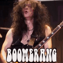 a man with long curly hair is playing a guitar in front of a boomerang sign .