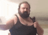 a bearded man in a black tank top is holding a microphone in his hand .