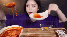 a woman in a purple shirt is eating a bowl of food with a spoon in her mouth .