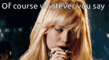 a blonde woman singing into a microphone with the words of course whatever you say behind her