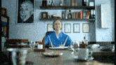 a woman in a blue shirt sits at a desk with a picture of albert einstein on the wall behind her