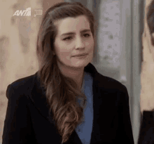 a woman wearing a black coat and a blue shirt is standing in front of a wall .