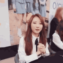 a woman with long red hair is sitting at a table with her hands folded in front of a group of girls .