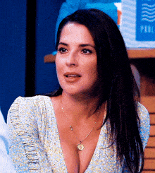 a woman wearing a necklace and a plunging neckline is sitting in front of a table .