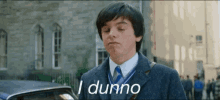 a young man in a suit and tie says i dunno in front of a building .