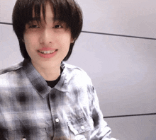 a young man wearing a plaid shirt is smiling and looking at the camera