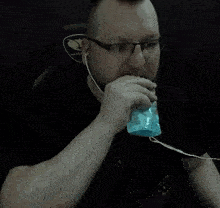 a man wearing glasses and earbuds is drinking from a bag .