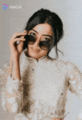 a woman wearing sunglasses and a white top has a tattoo on her wrist that says ' gocut '