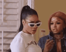 a woman wearing sunglasses is standing next to another woman .