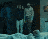 a group of people are standing around a person laying on a bed .