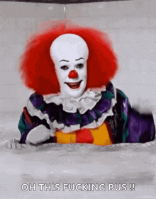 a clown with red hair and a red nose is laying on a table .