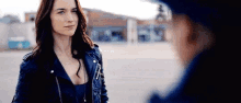 a woman in a blue leather jacket is standing next to a man in a blue hat .