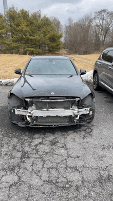 a black car with a damaged front bumper is parked in a parking lot