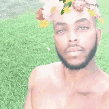 a shirtless man with a beard and a flower crown on his head is taking a selfie in a park .