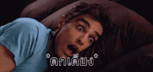a man in a blue shirt is laying on a couch with his mouth open in a foreign language .