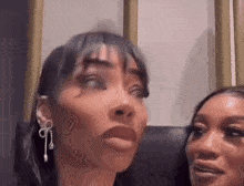 two women are sitting next to each other on a couch and looking at the camera .