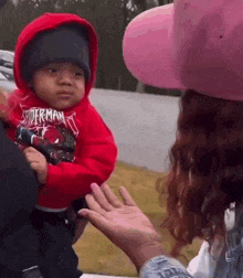 a woman is holding a baby in her arms and the baby is wearing a spiderman sweatshirt .