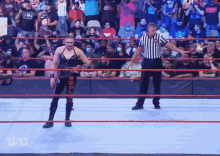 a female wrestler is standing in a wrestling ring with a referee in front of a crowd .