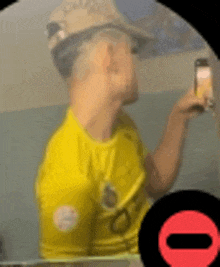 a man wearing a yellow shirt and a hat is taking a selfie with his cell phone .