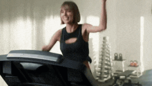 a woman is riding a treadmill in a gym with her hand in the air .