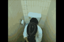 a woman is sitting on a toilet in a bathroom with a bun in her hair .