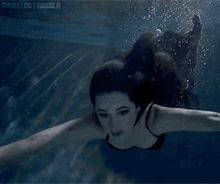 a woman in a black swimsuit is swimming underwater in a swimming pool