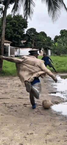 a man in a trench coat is kicking a soccer ball in the dirt