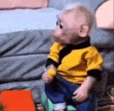 a baby monkey is sitting on a couch wearing a yellow jacket and blue jeans .