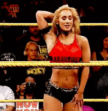 a woman in a red top and black shorts is standing in a wrestling ring
