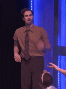 a man in a brown shirt and tie stands in front of a blue curtain