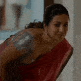 a woman in a red saree is sitting on a chair and looking down .