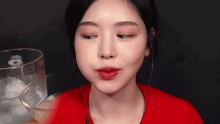 a woman in a red shirt is drinking a glass of water .