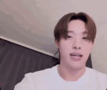 a young man is wearing a white t-shirt and looking at the camera in a room .