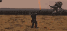 a man is standing in the middle of a field with a sword in his hand surrounded by fire .
