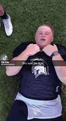 a man in a spartan jersey is laying on the grass with his hands on his chest .