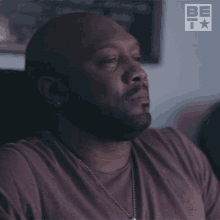 a man in a purple shirt is sitting in front of a sign that says be t
