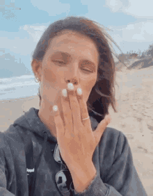 a woman blowing a kiss on a beach with her hand