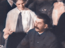 a man with a mustache is standing next to a woman in a white shirt and tie .